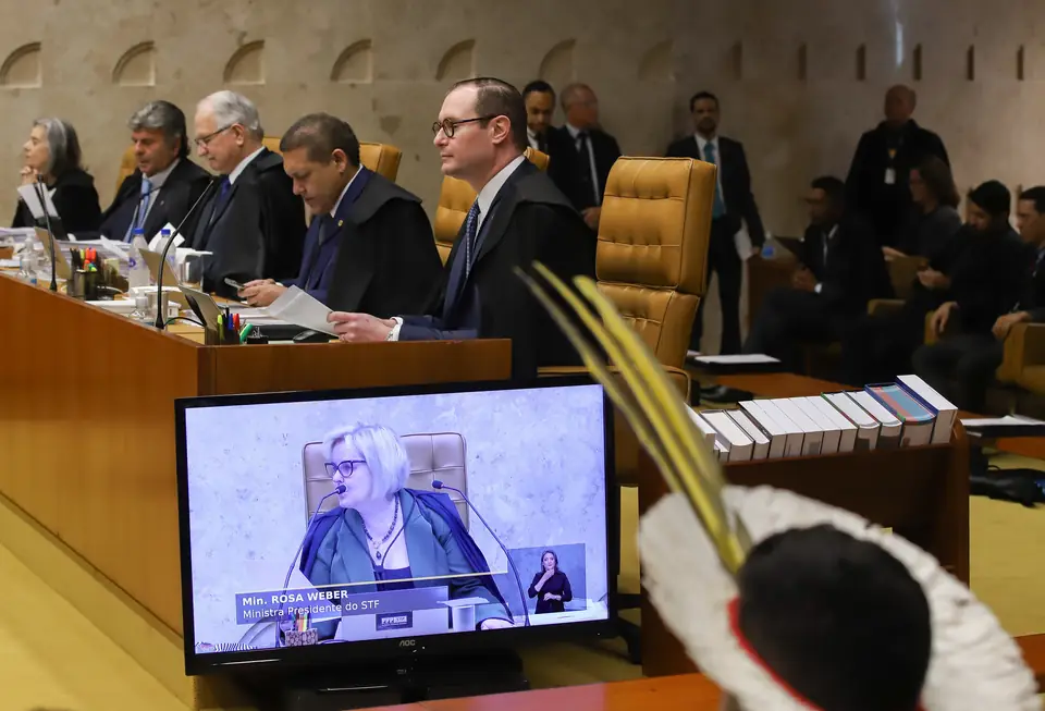 Ministros do STF na bancada, com a presidente Rosa Weber no telão e um cocar indígena em primeiro plano, no julgamento do marco temporal, 21 de setembro de 2023